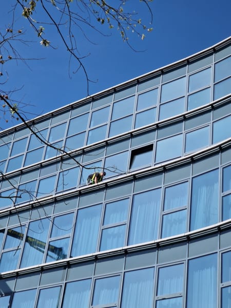 Mitarbeiter reinigt eine geschwungene Glasfassade vom Fassadenband aus