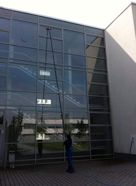 Mitarbeiter von Clean Gebäudemanagement reinigt die hohe Glasfassade eines Schulgebäudes mit einer Teleskop-Wasserstange